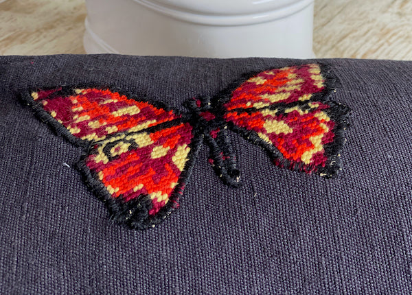 détail coussin décoratif en lin ancien teint noir et canevas recyclé motif papillon rouge et jaune appliqué au surjet